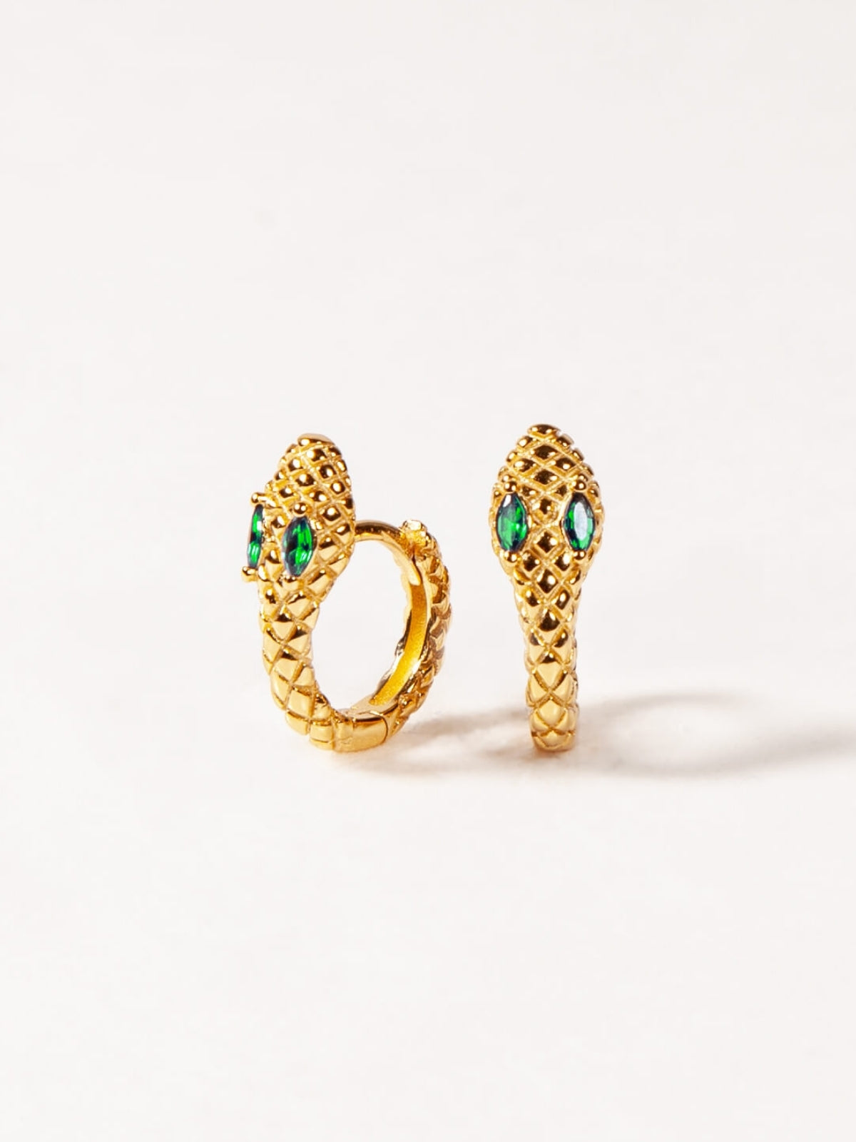 Gold snake-shaped earrings with green gemstones on a white background