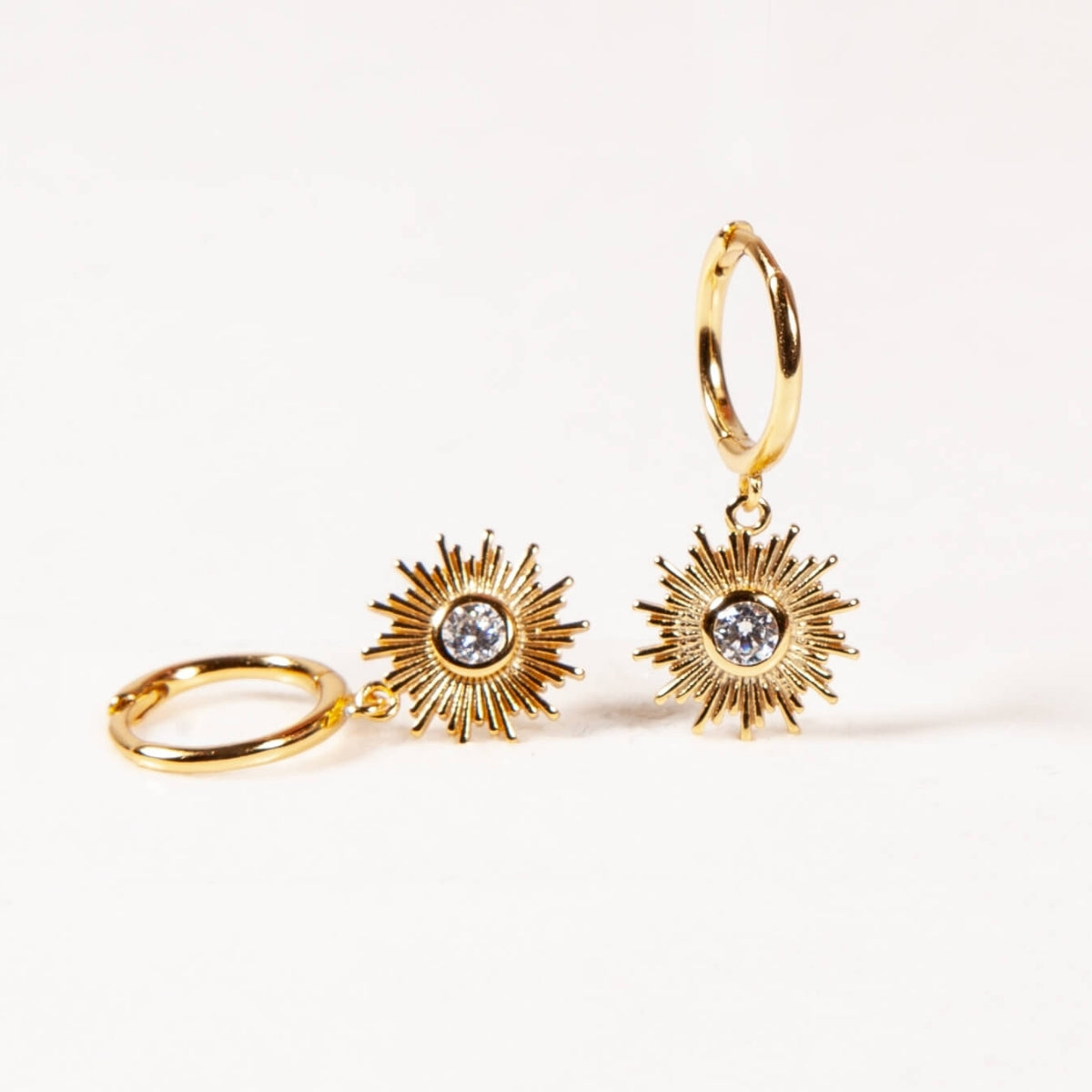 Gold hoop earrings with sunburst designs and clear gemstones on a white background