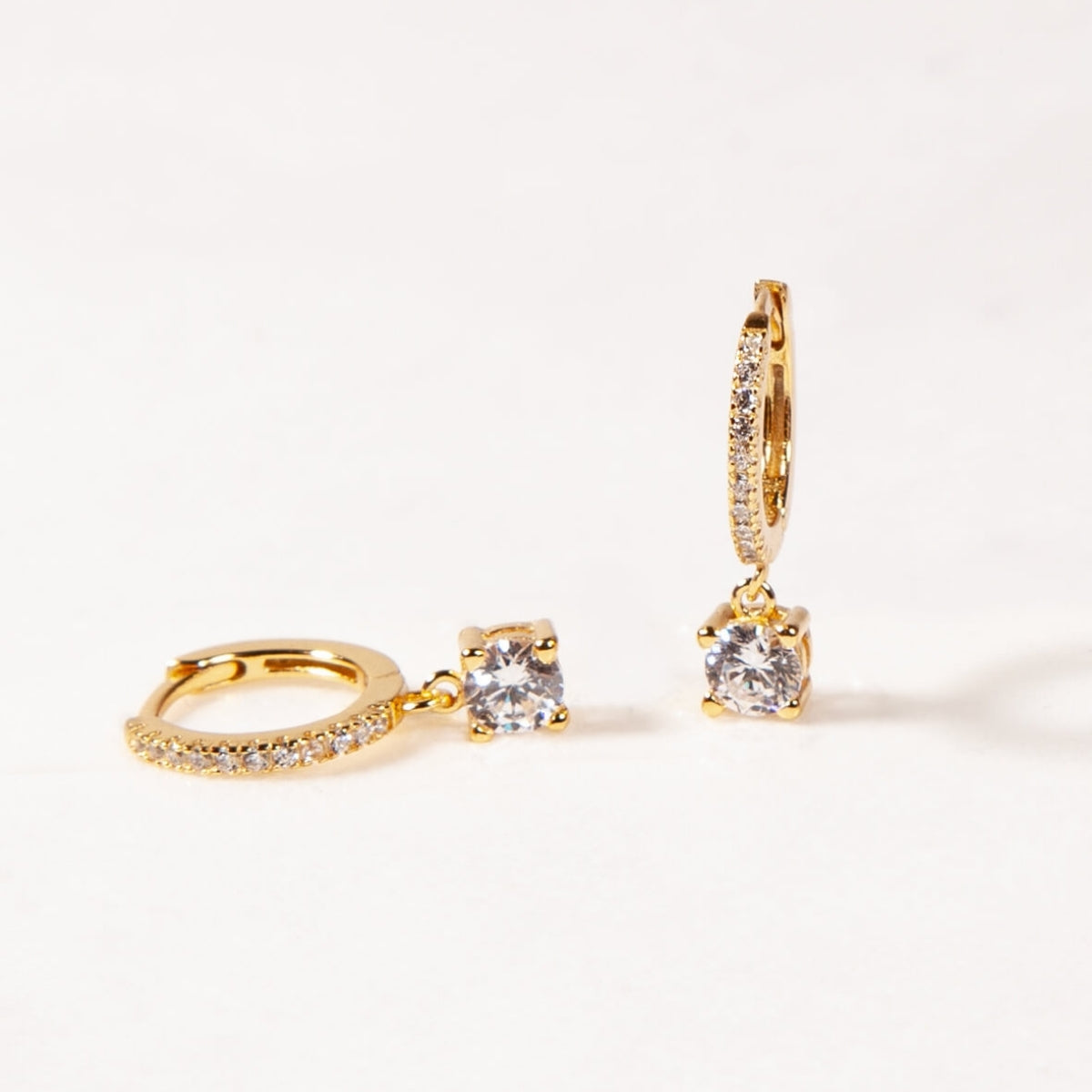 Gold hoop earrings with clear gemstones on a light beige background