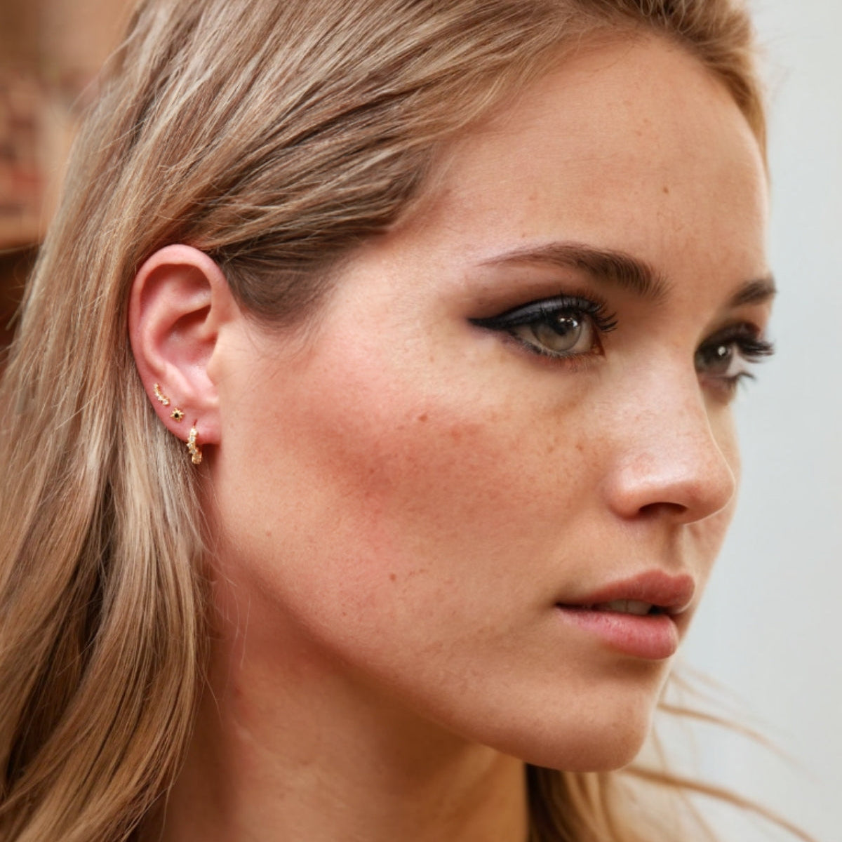 Close-up of a woman with blonde hair and freckles, wearing a small earring.