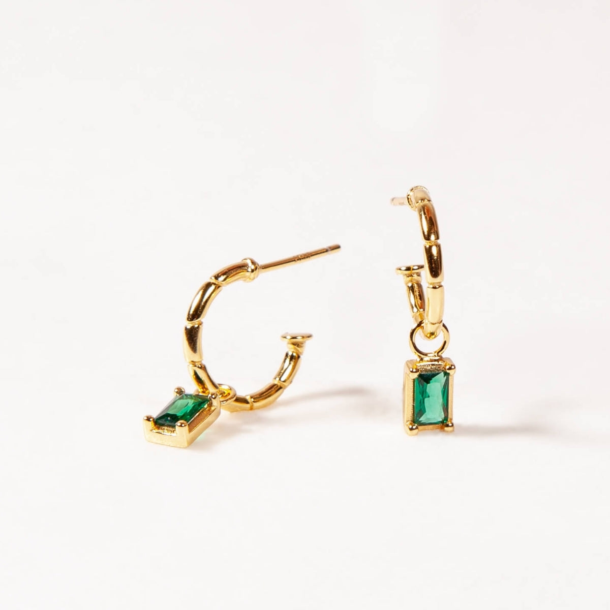 Gold hoop earrings with green gemstones on a white background