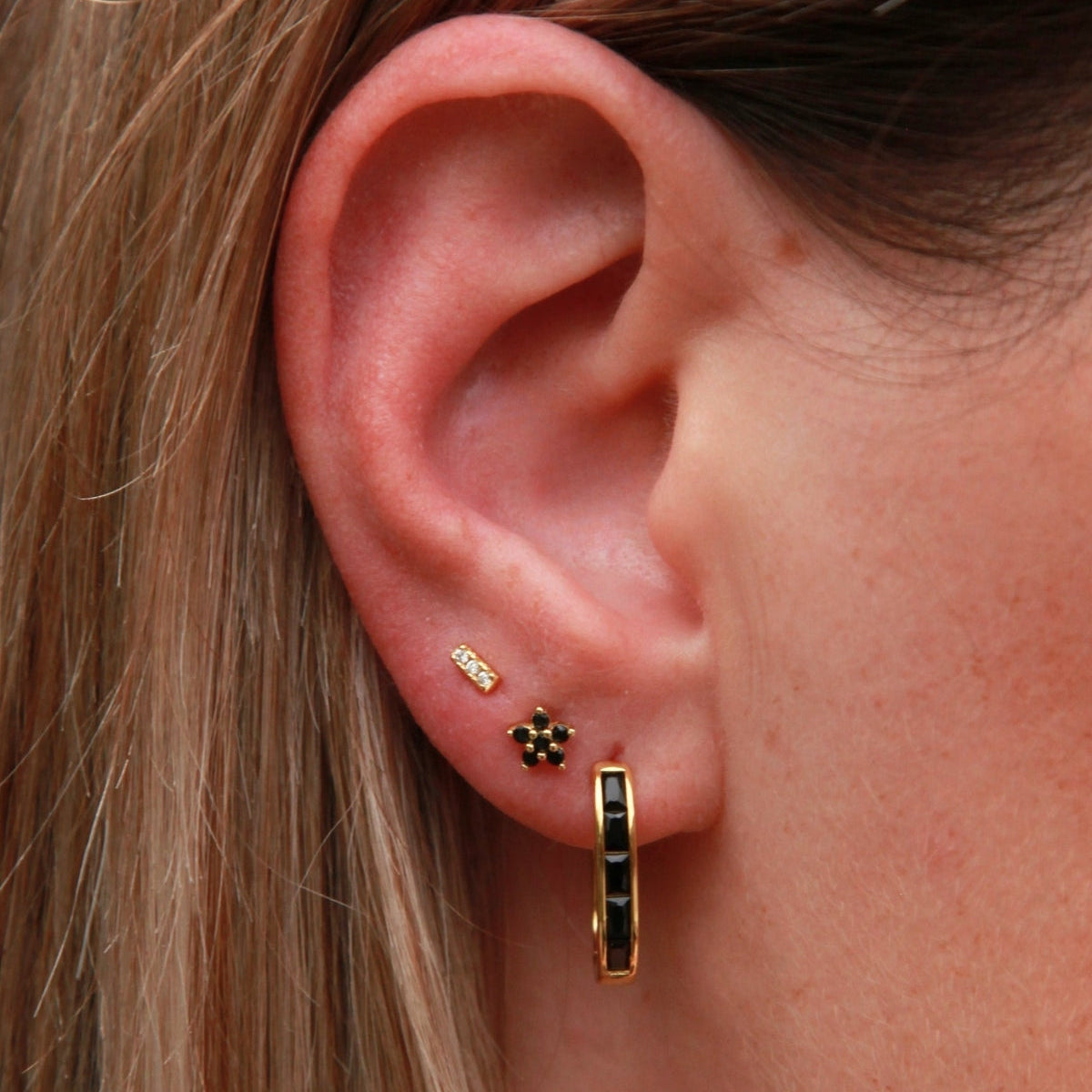 Close-up of an ear wearing gold hoop earrings with a small black stone.