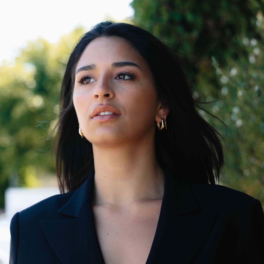 a woman wearing black suit with black hair wearing gold earrings