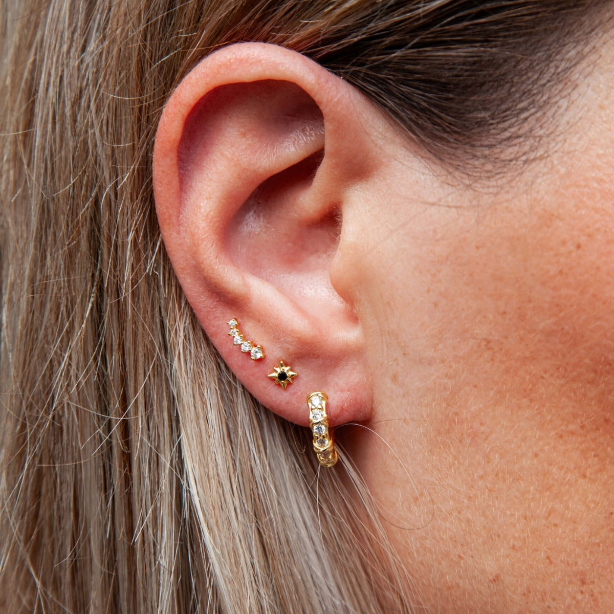Close-up of an ear with gold hoop earrings and a small stud.