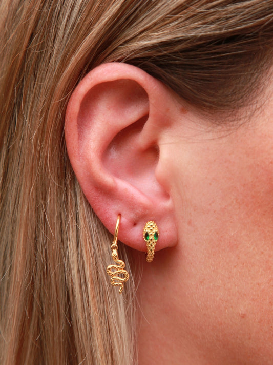Close-up of a person wearing gold hoop earrings with green gemstones.