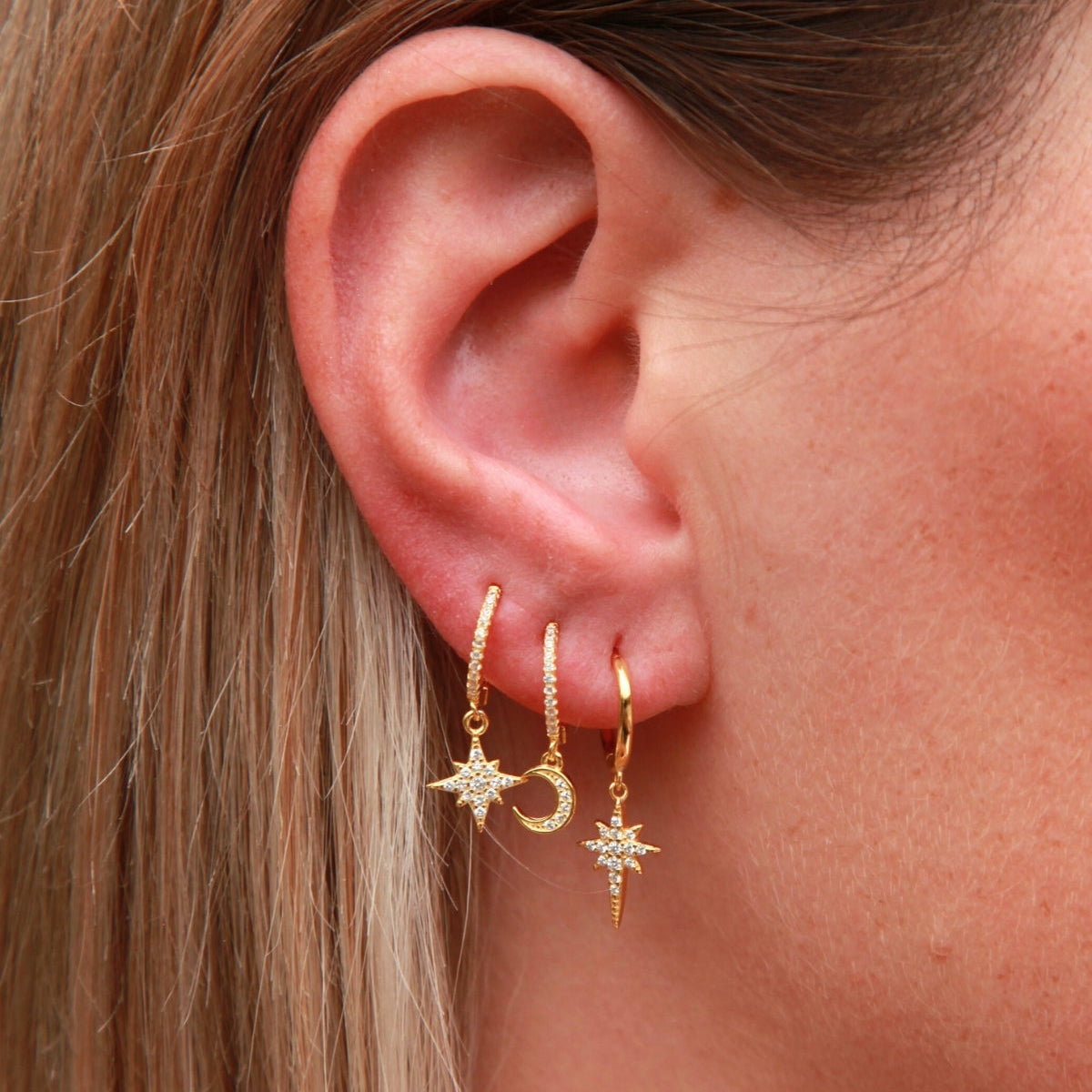 Close-up of an ear wearing gold earrings with star and moon designs.