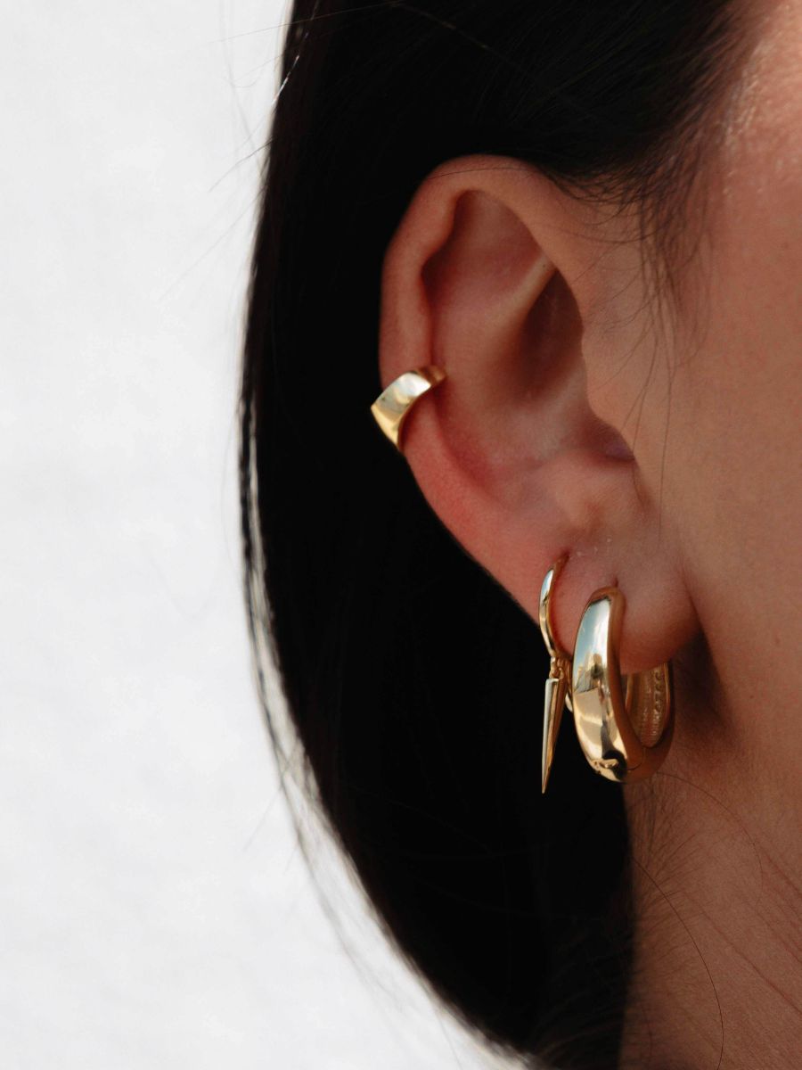 a woman with black hair and she is wearing bar dangle huggies.