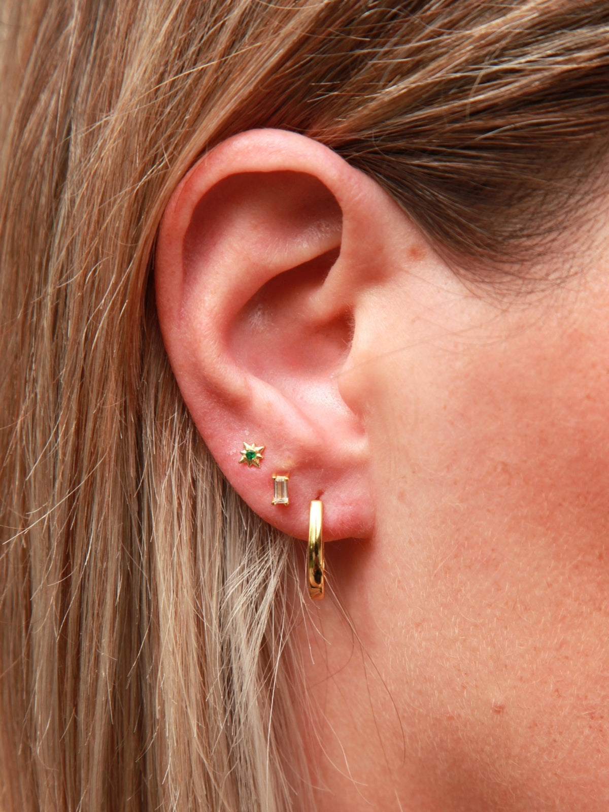 Close-up of an ear wearing gold hoop earrings with a green gemstone.