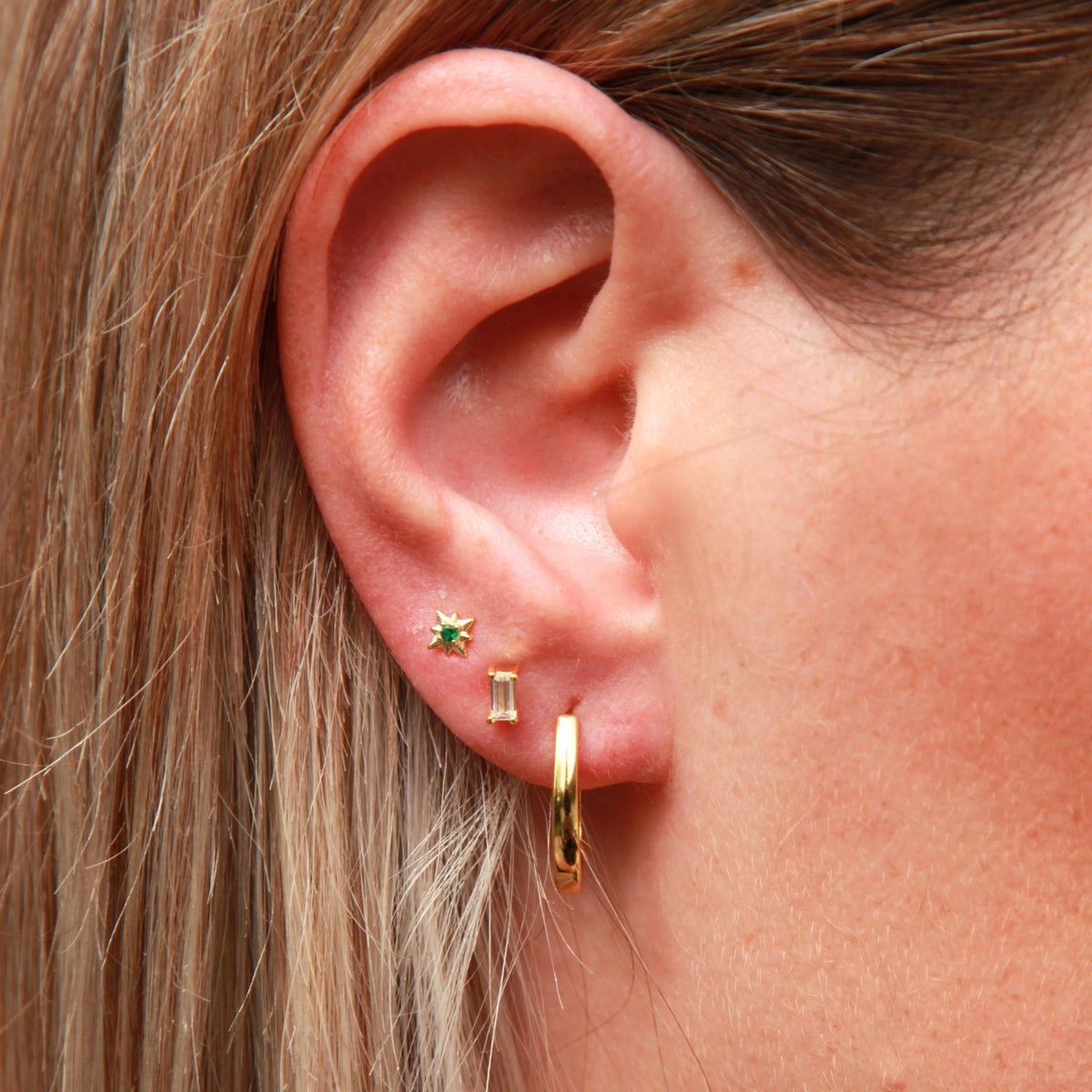 Close-up of an ear wearing gold hoop earrings with a green gemstone.