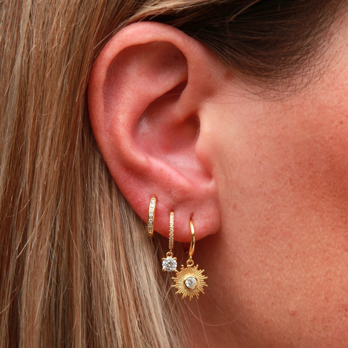 Close-up of an ear wearing gold hoop earrings with small gemstones.
