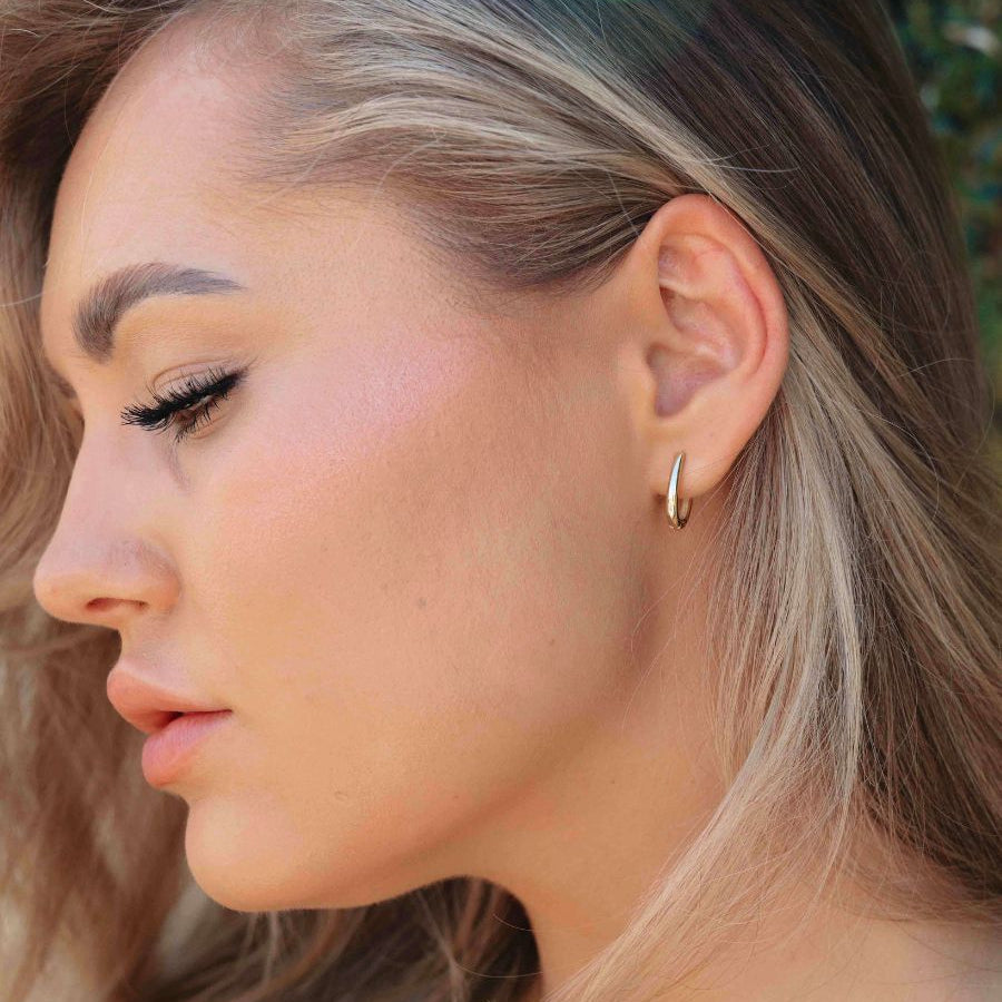 Close-up of an ear wearing gold oval hoop earrings