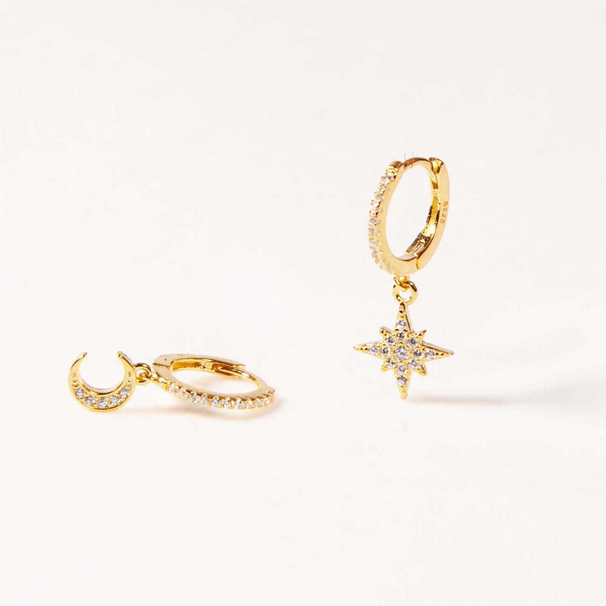 Gold hoop earrings with star and moon charms on a white background