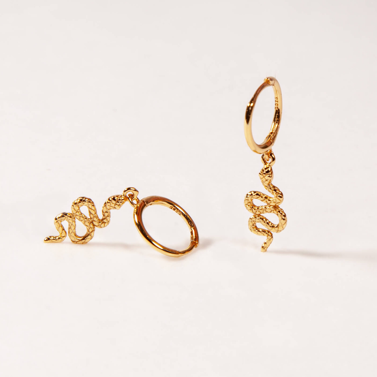 Gold snake-shaped earrings on a white background