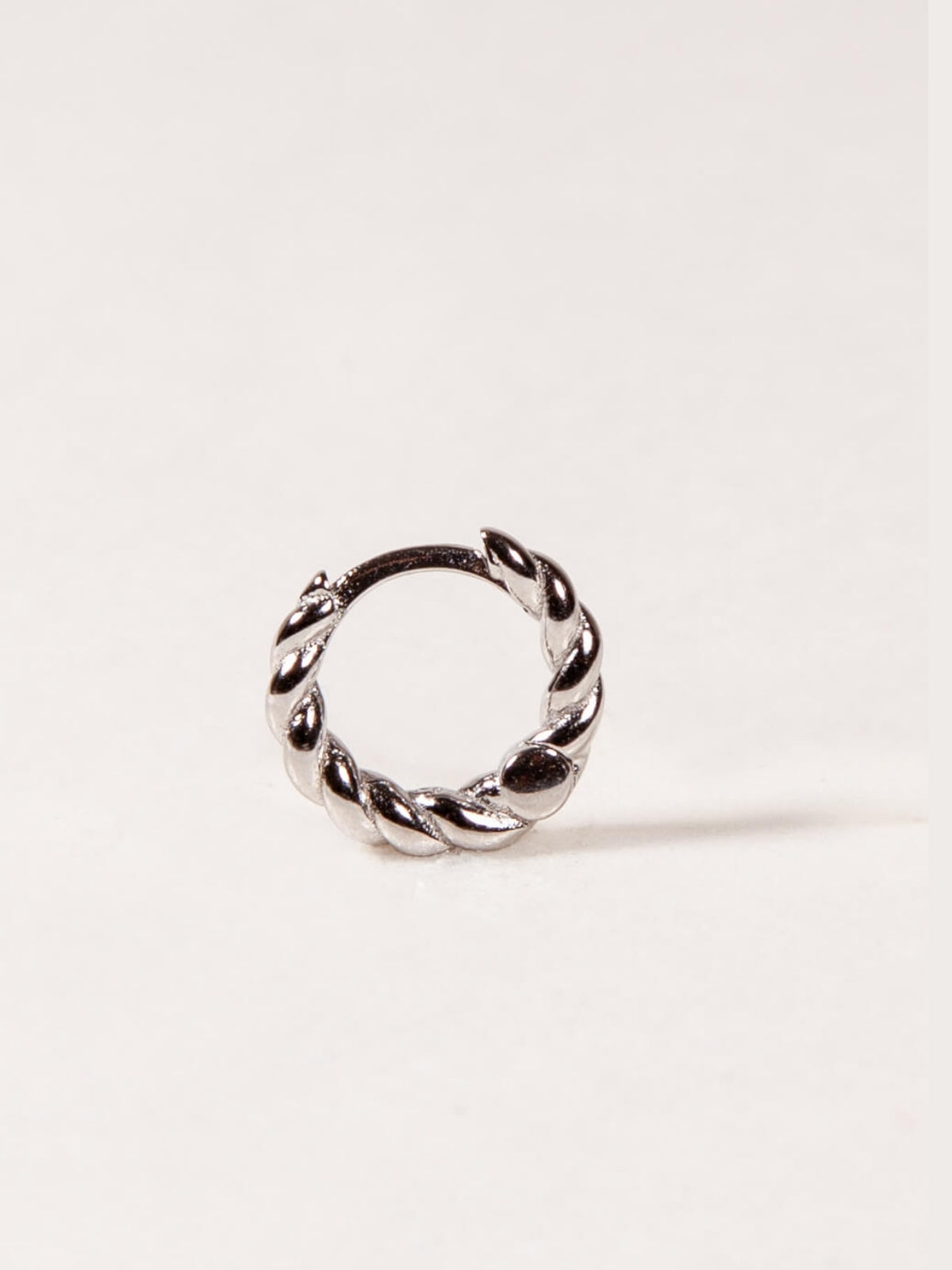 Silver twisted hoop earrings with a twisted design on a light pink background