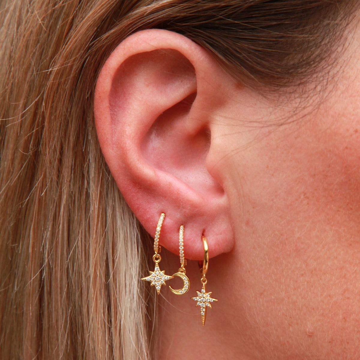 Close-up of an ear wearing gold earrings with star and moon designs.