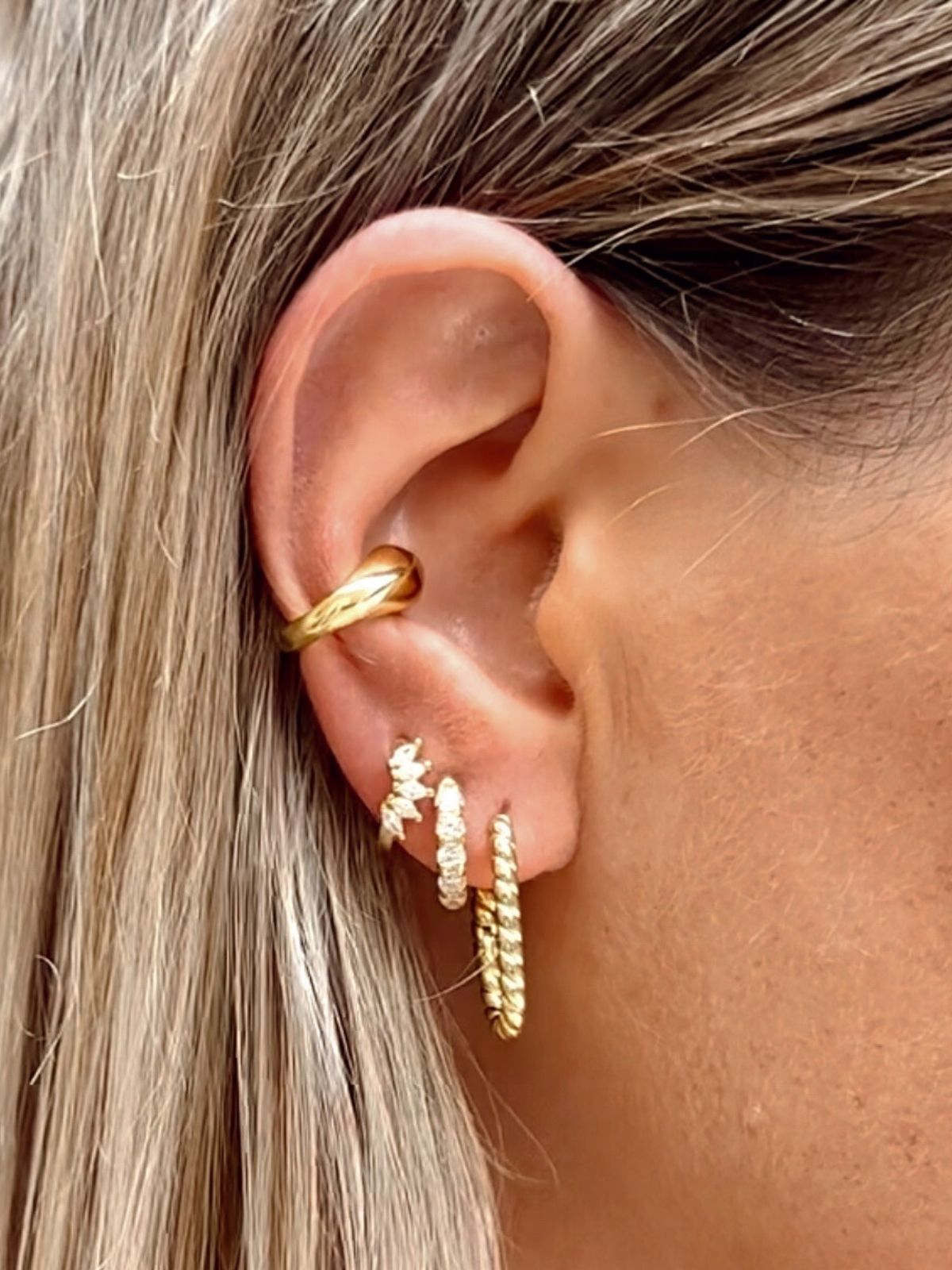 Close-up of an ear wearing gold hoop earrings with a blurred background