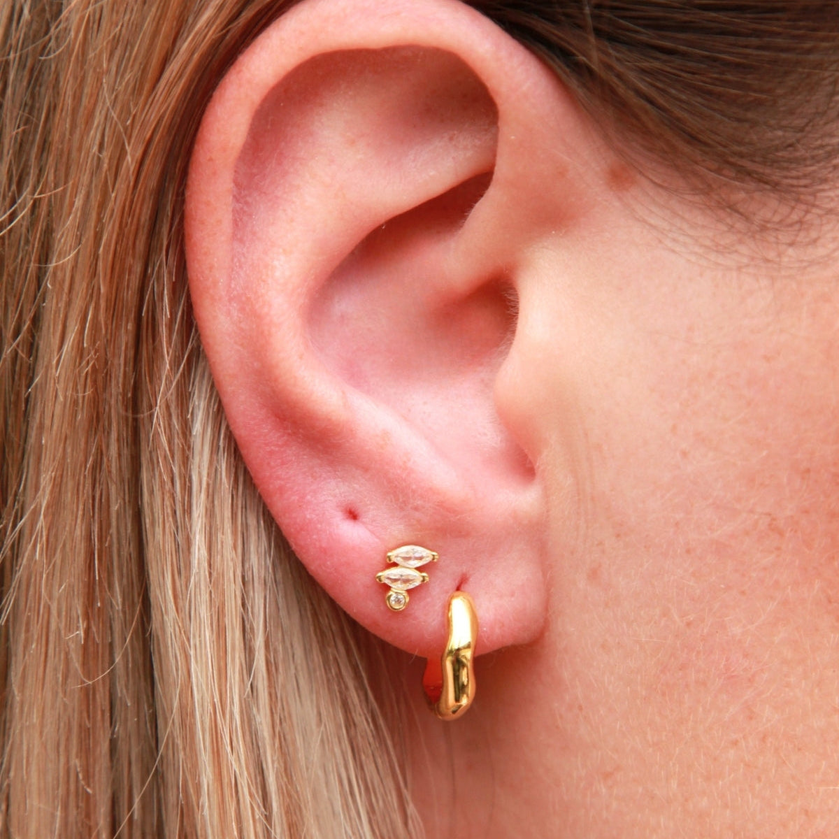 Close-up of a person wearing gold hoop earrings and marquise cut stud with a blurred background