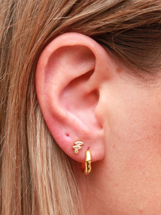 Close-up of a person wearing gold hoop earrings and marquise cut stud with a blurred background
