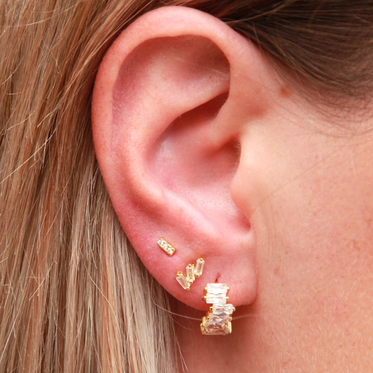 Close-up of an ear wearing gold earrings with a neutral background