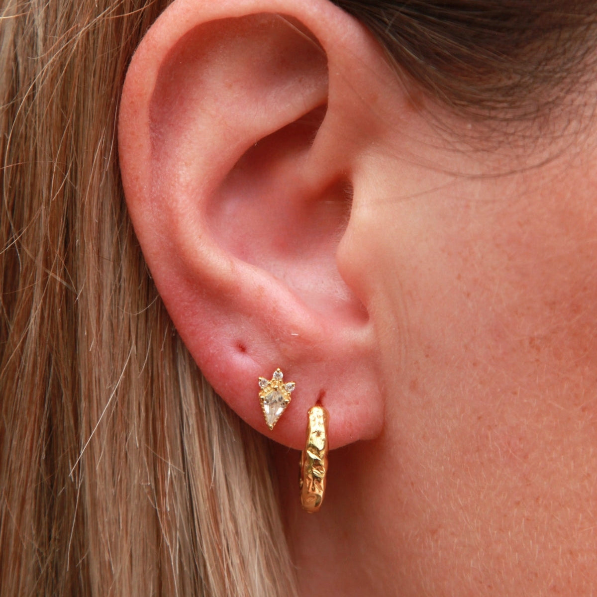 Close-up of an ear wearing gold hoop earrings and a kite shape stud.