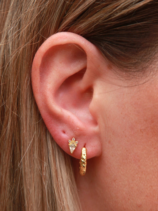 Close-up of an ear wearing gold hoop earrings and a kite shape stud.