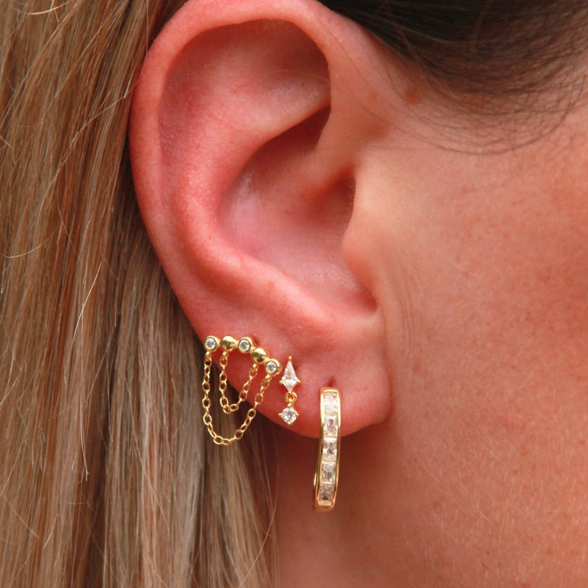 Close-up of an ear wearing gold earrings with a blurred background