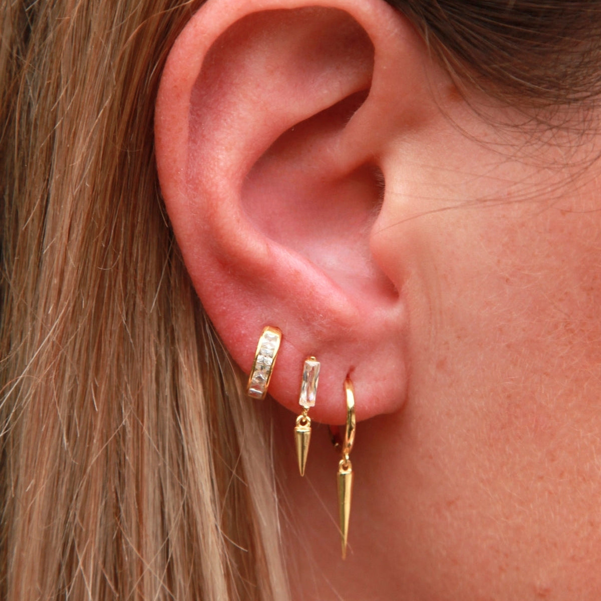Close-up of an ear wearing gold hoop earrings with a blurred background