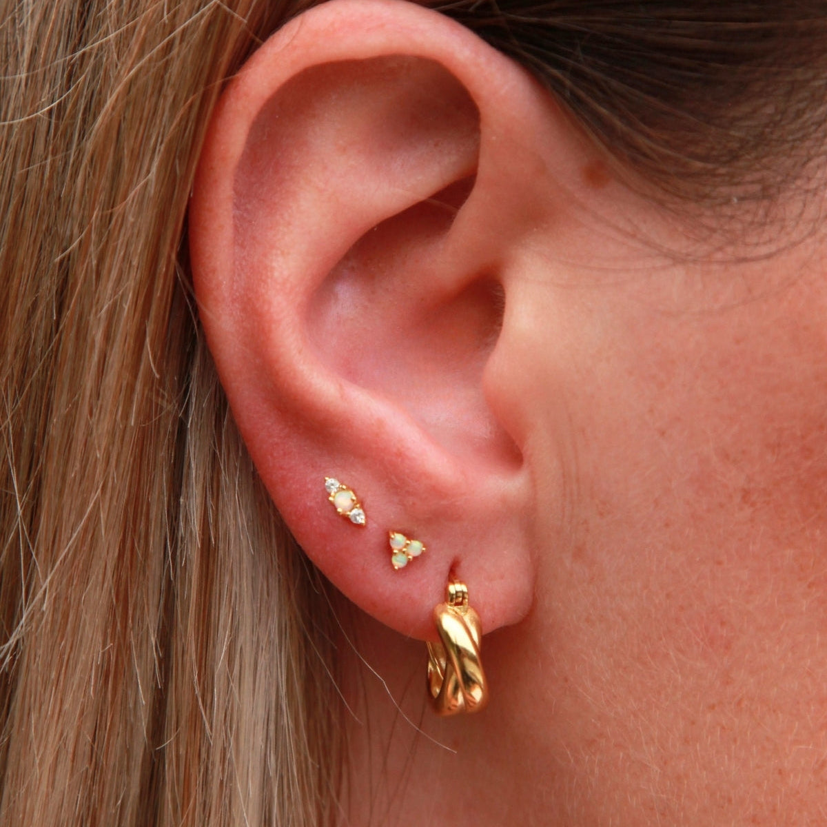 Close-up of an ear wearing gold earrings with blonde hair.