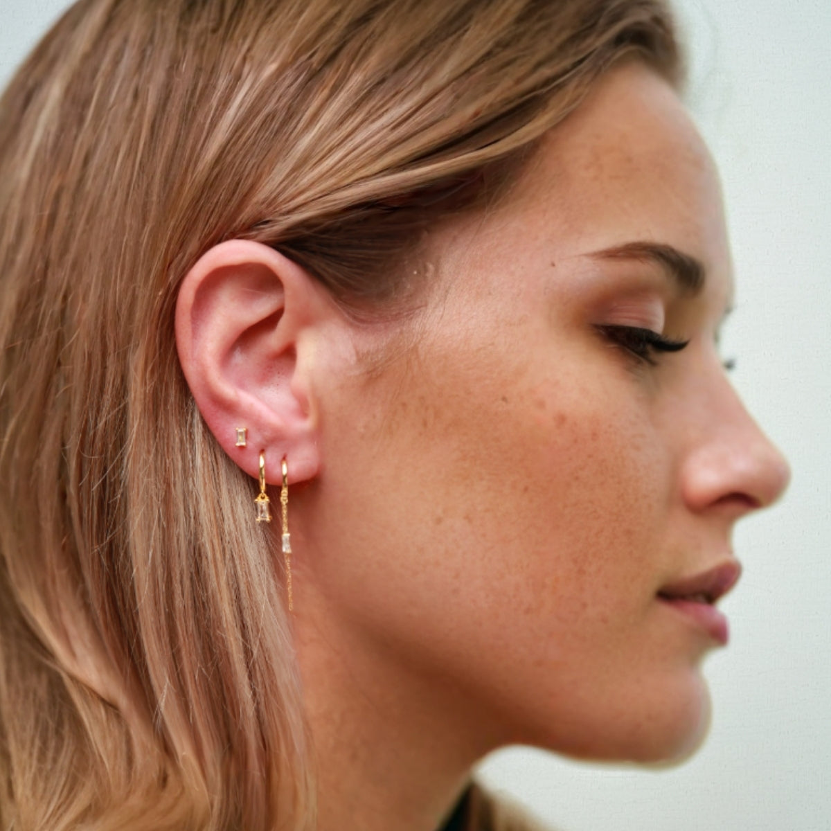 Close-up of a woman wearing gold earrings with a neutral background