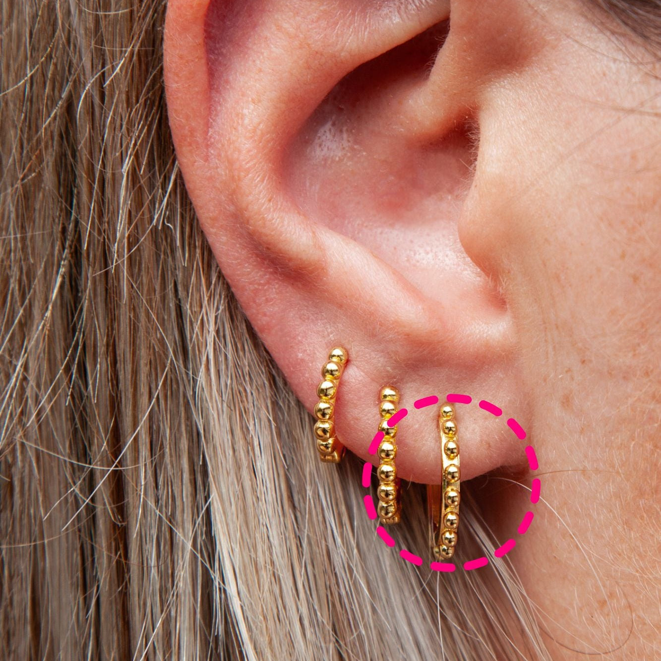 A woman wearing three hoops with bead details