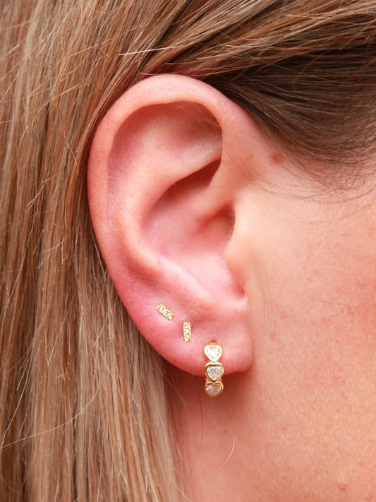 Close-up of an ear wearing gold earrings with blonde hair.