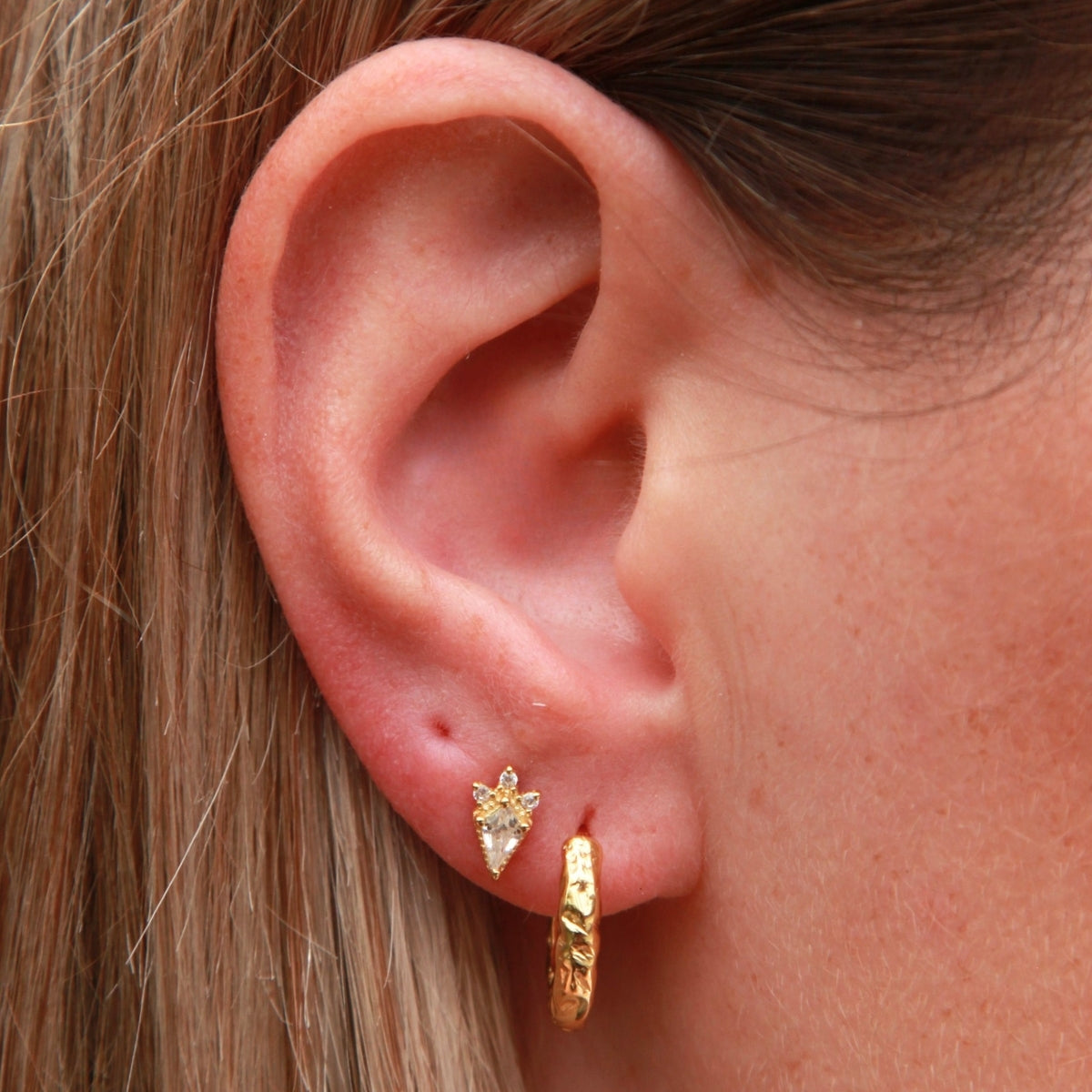 Close-up of an ear wearing gold hoop earrings with a star detail.