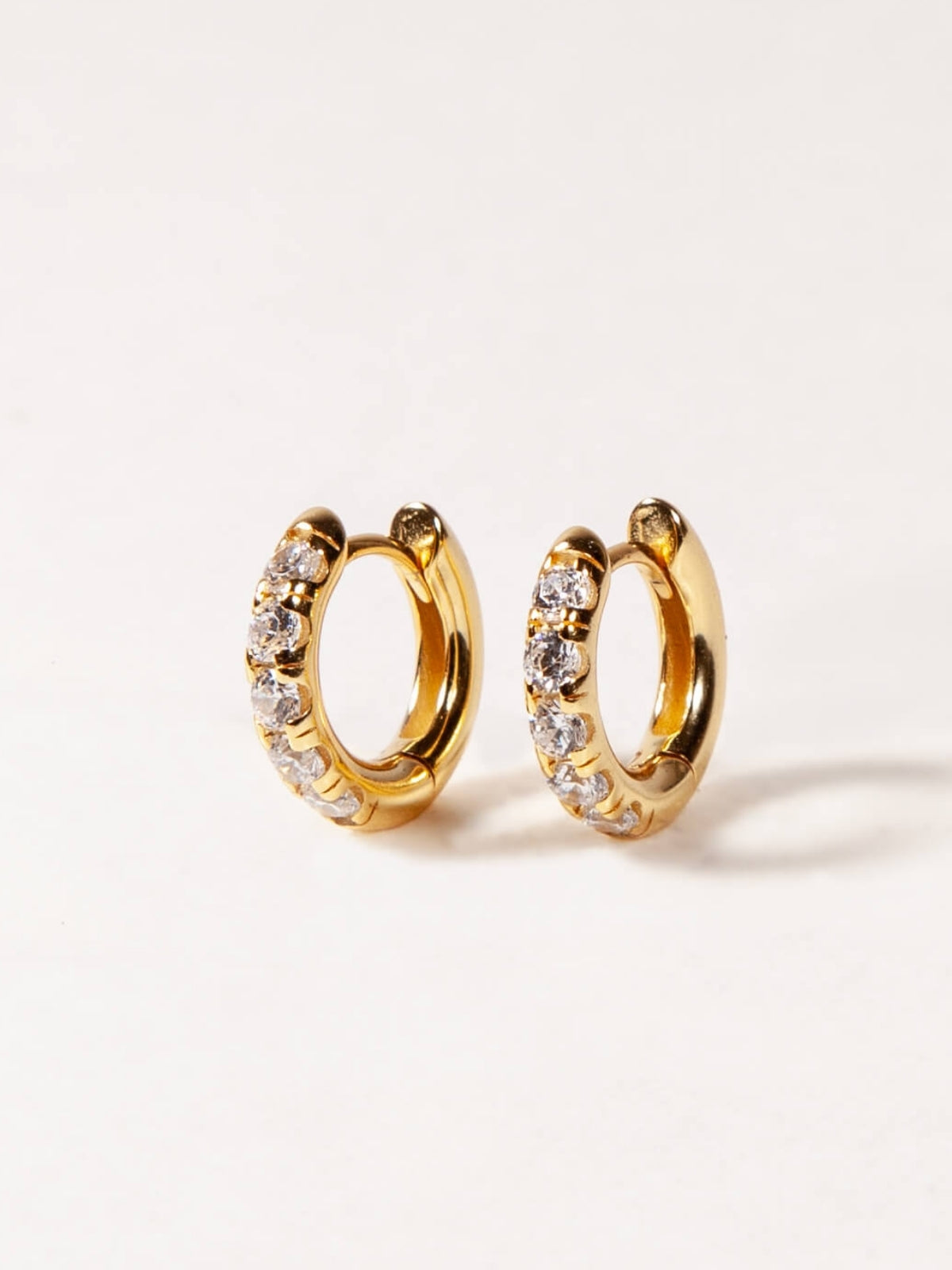 Gold hoop earrings with embedded stones on a light gray background