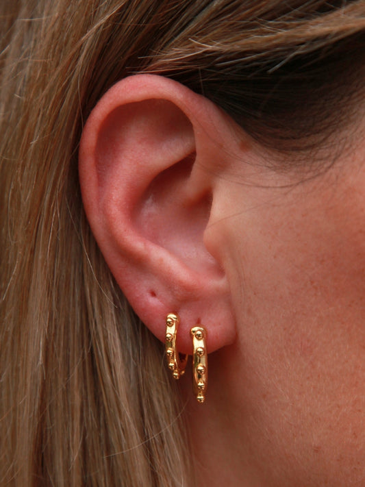 Close-up of an ear wearing gold hoop earrings with hair partially covering the frame.