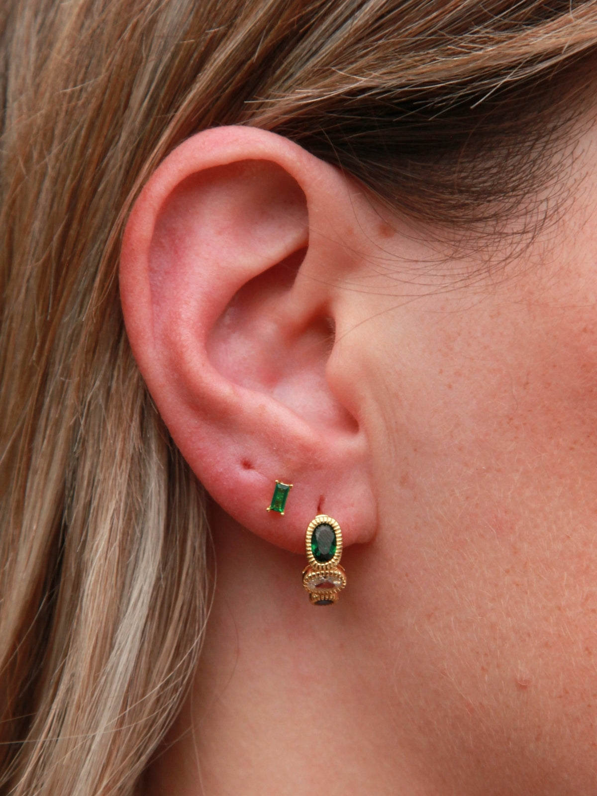 Close-up of an ear wearing a gold earring with green gemstone.