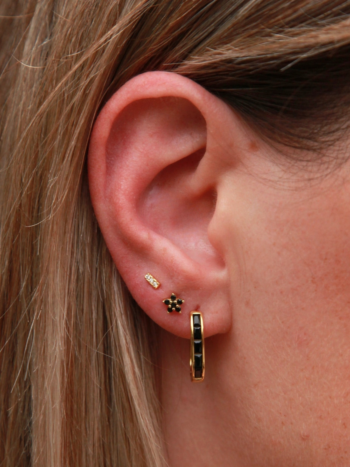 Close-up of an ear wearing gold U shape hoop earrings with a small black stone.