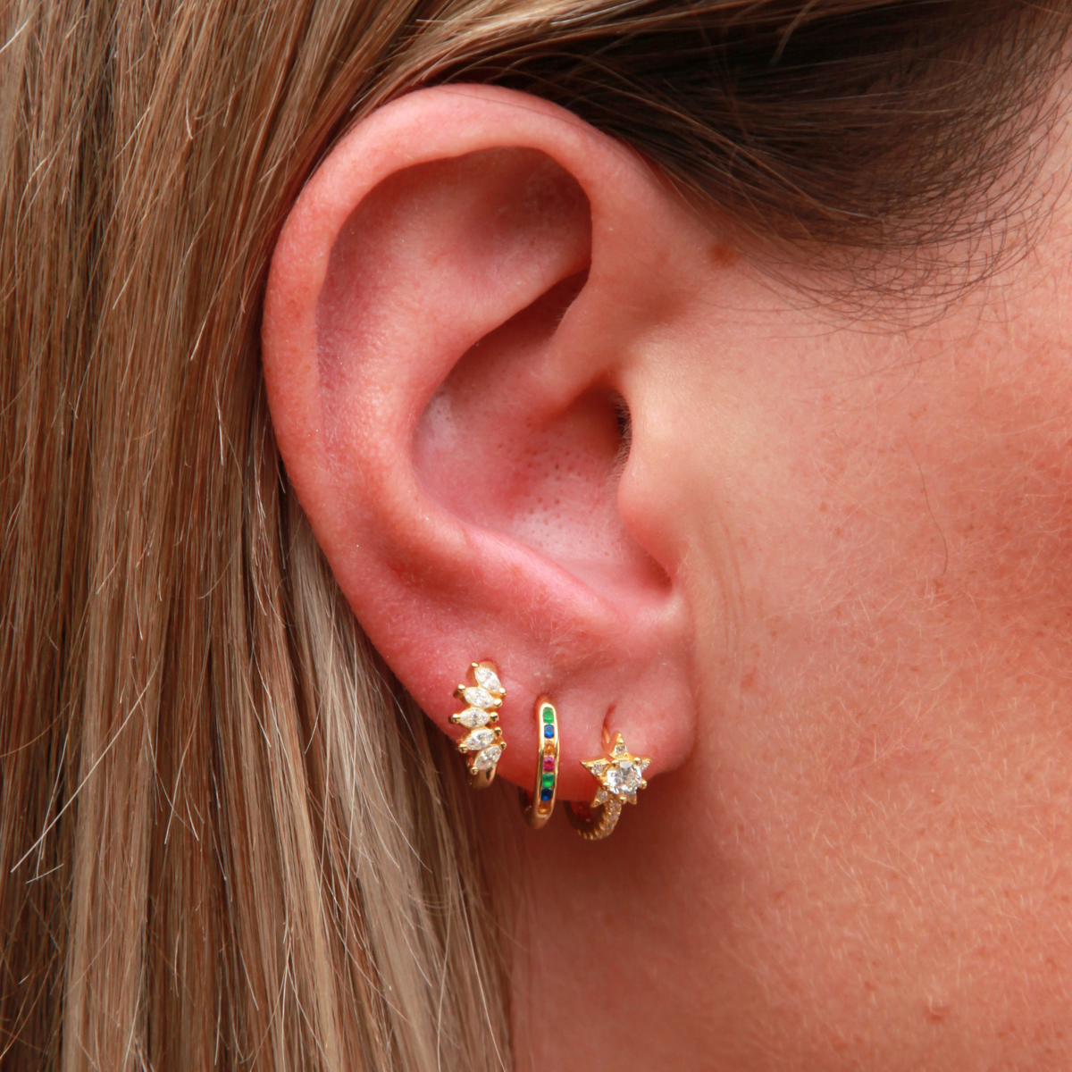 Close-up of an ear wearing a gold earring with colorful gemstones.