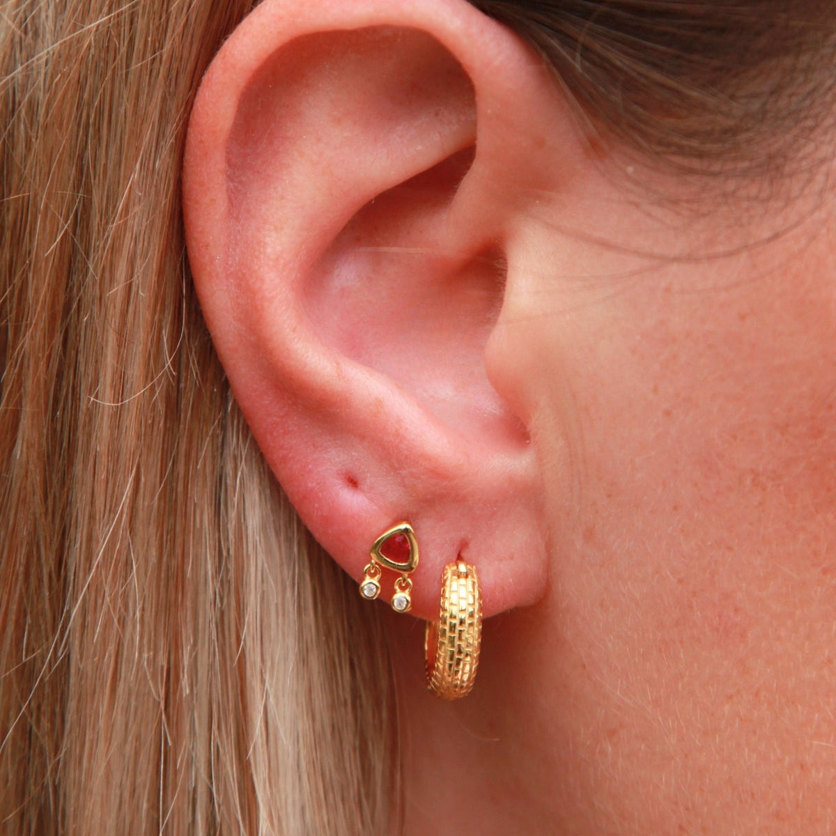 Close-up of an ear wearing gold hoop earrings with a red gemstone.