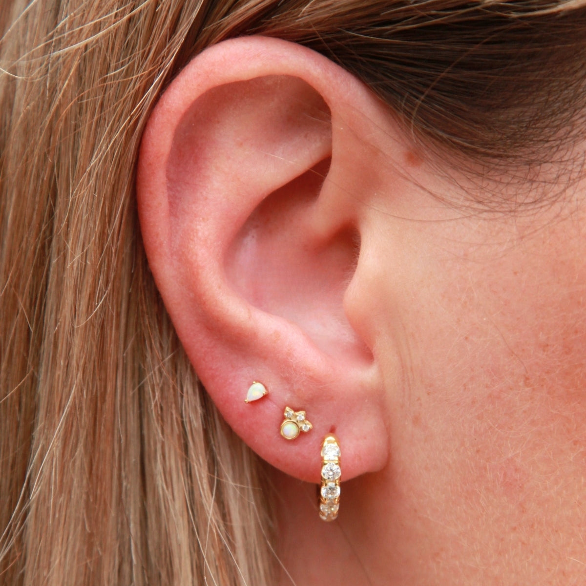 Close-up of an ear wearing gold earrings with blonde hair.