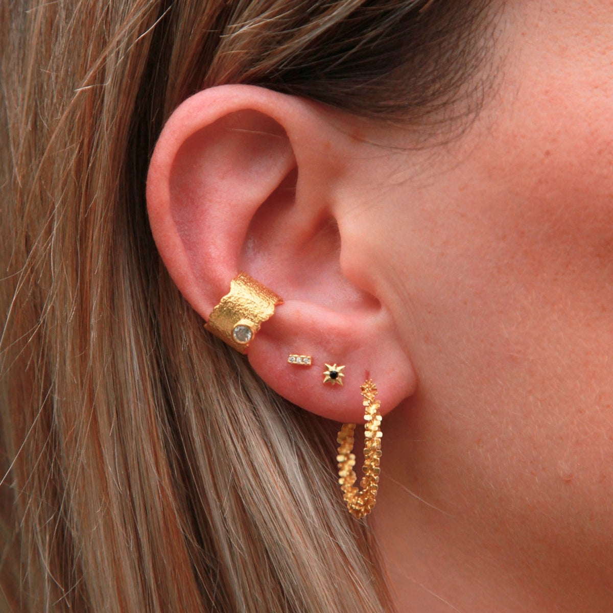 Close-up of an ear with gold earrings and a textured cuff.