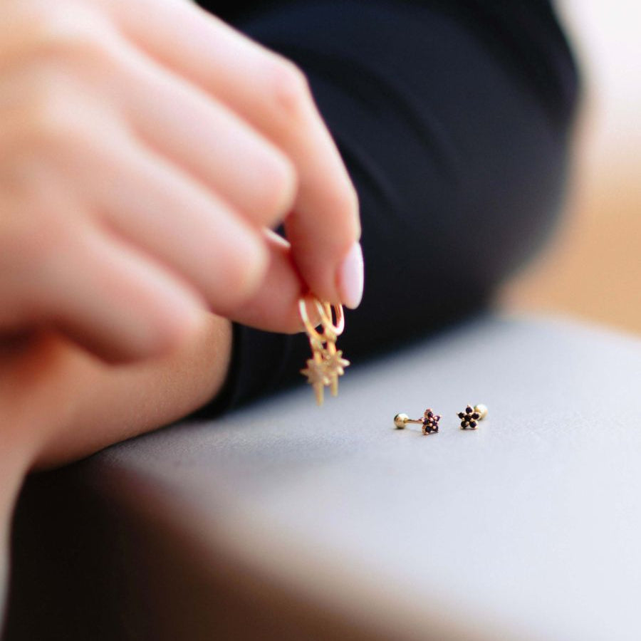 a woman holding a pair of star huggies and a floral studs