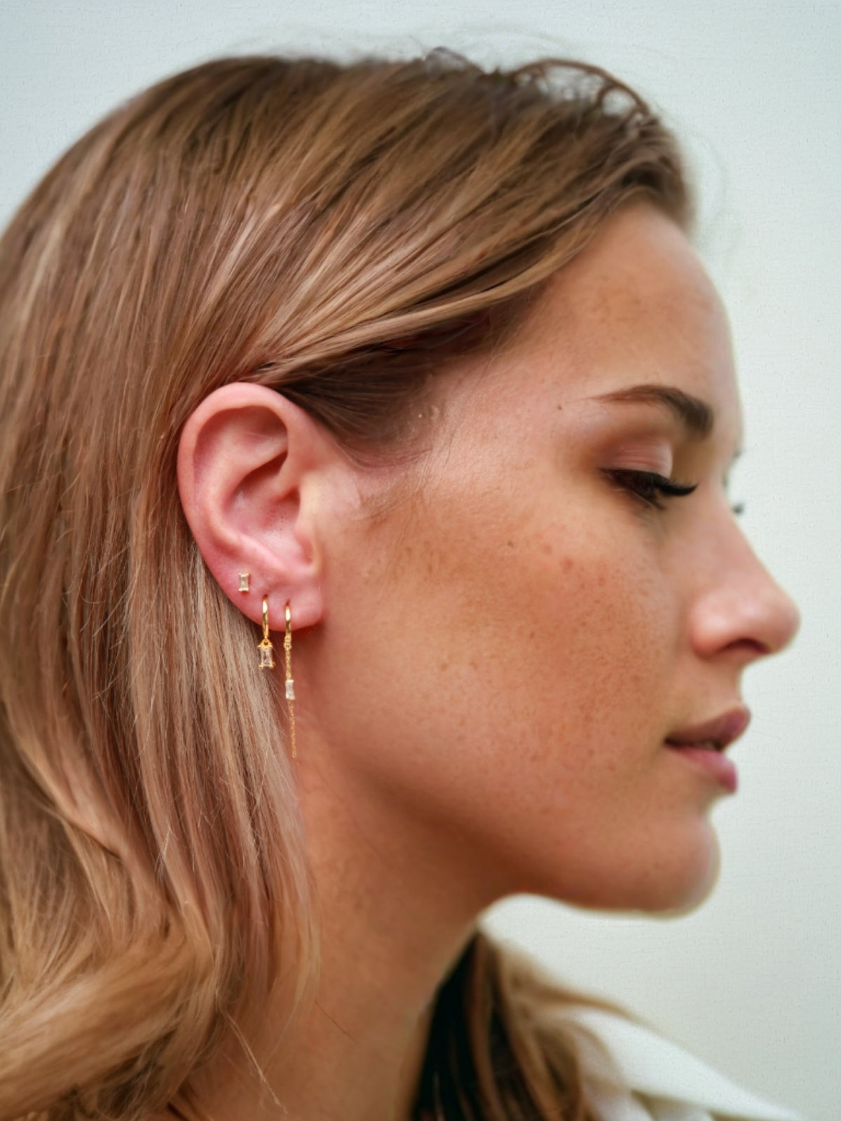 Close-up of a person wearing gold earrings with small baguette CZ Sones.