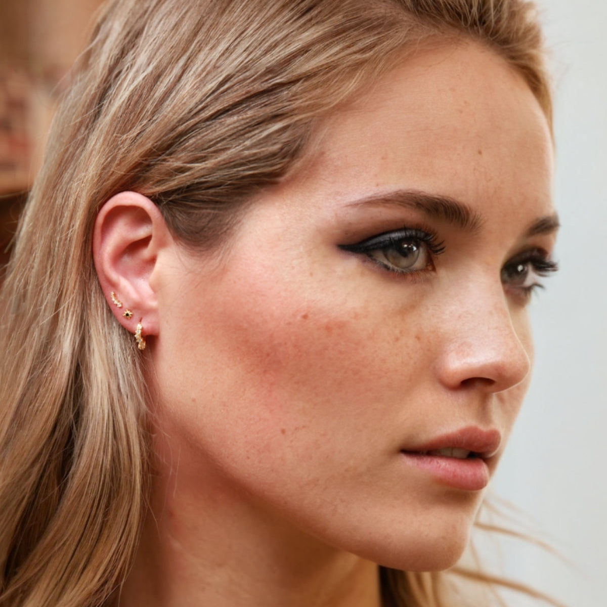Close-up of a woman with blonde hair and freckles, wearing stacked earrings, two star studs and CZ huggies.