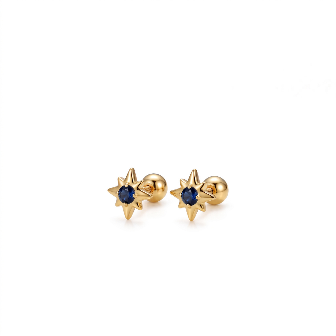 A pair of gold starburst stud earrings with a small dark blue gemstone in the center, set against a plain white background.