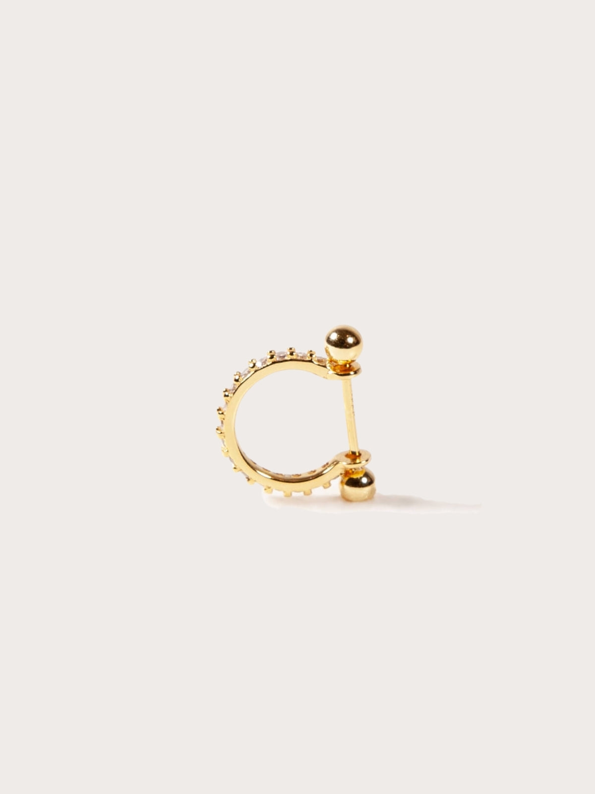 Gold hoop earring for helix or conch with embedded stones on a light beige background