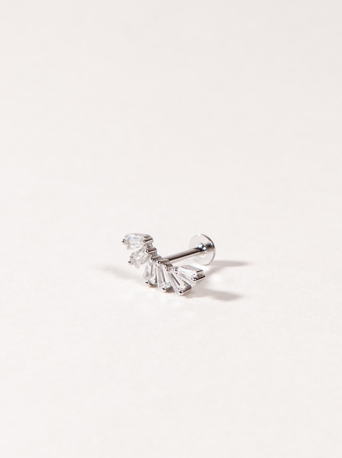 A Silver crown-like shape with baguette-cut stones stud earring on a light beige background