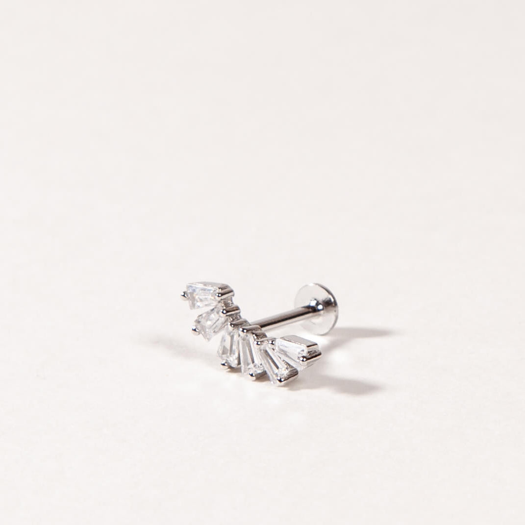 A Silver crown-like shape with baguette-cut stones stud earring on a light beige background