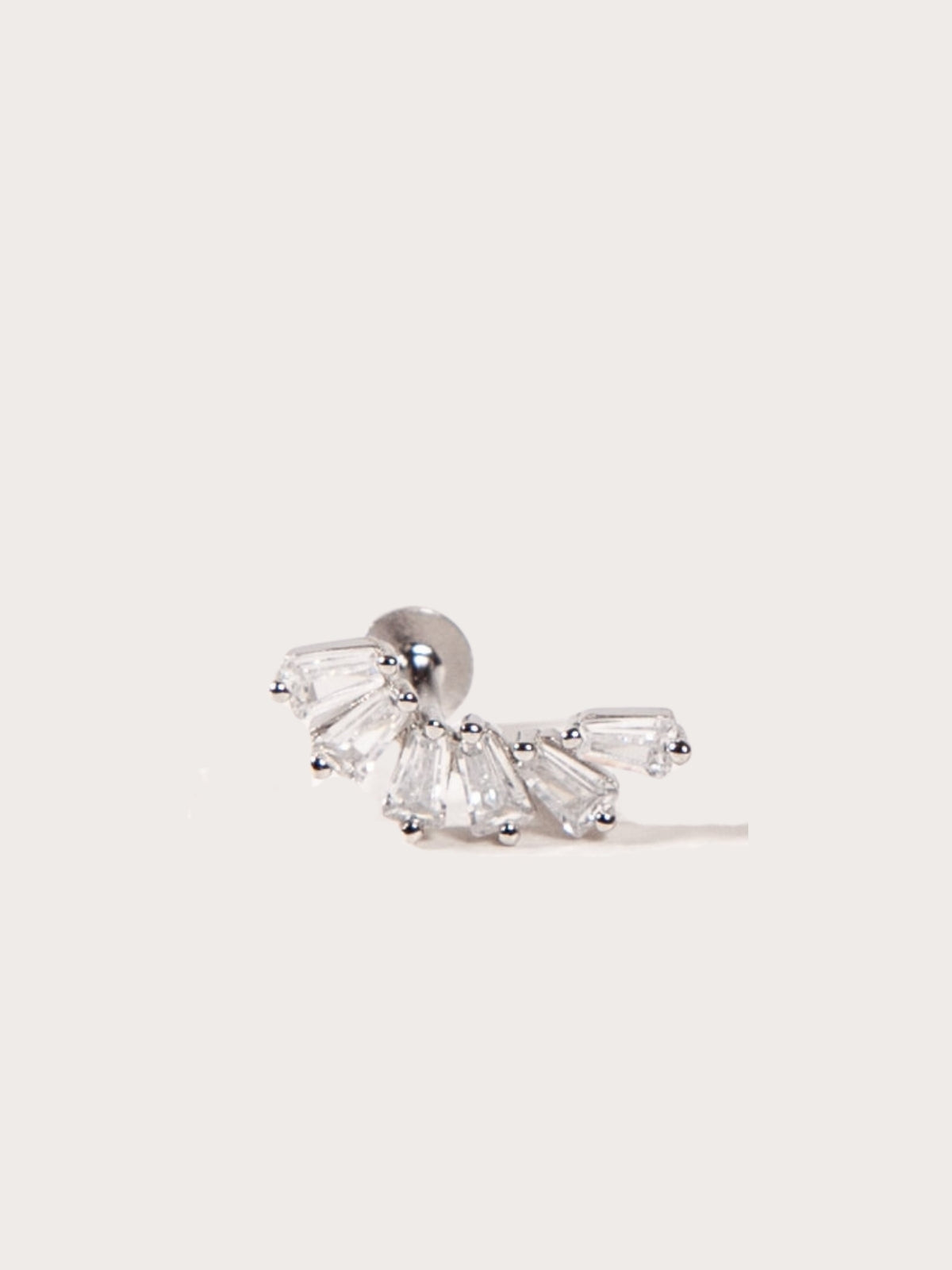 A silver crown-like shape with baguette-cut stones stud earring on a light beige background