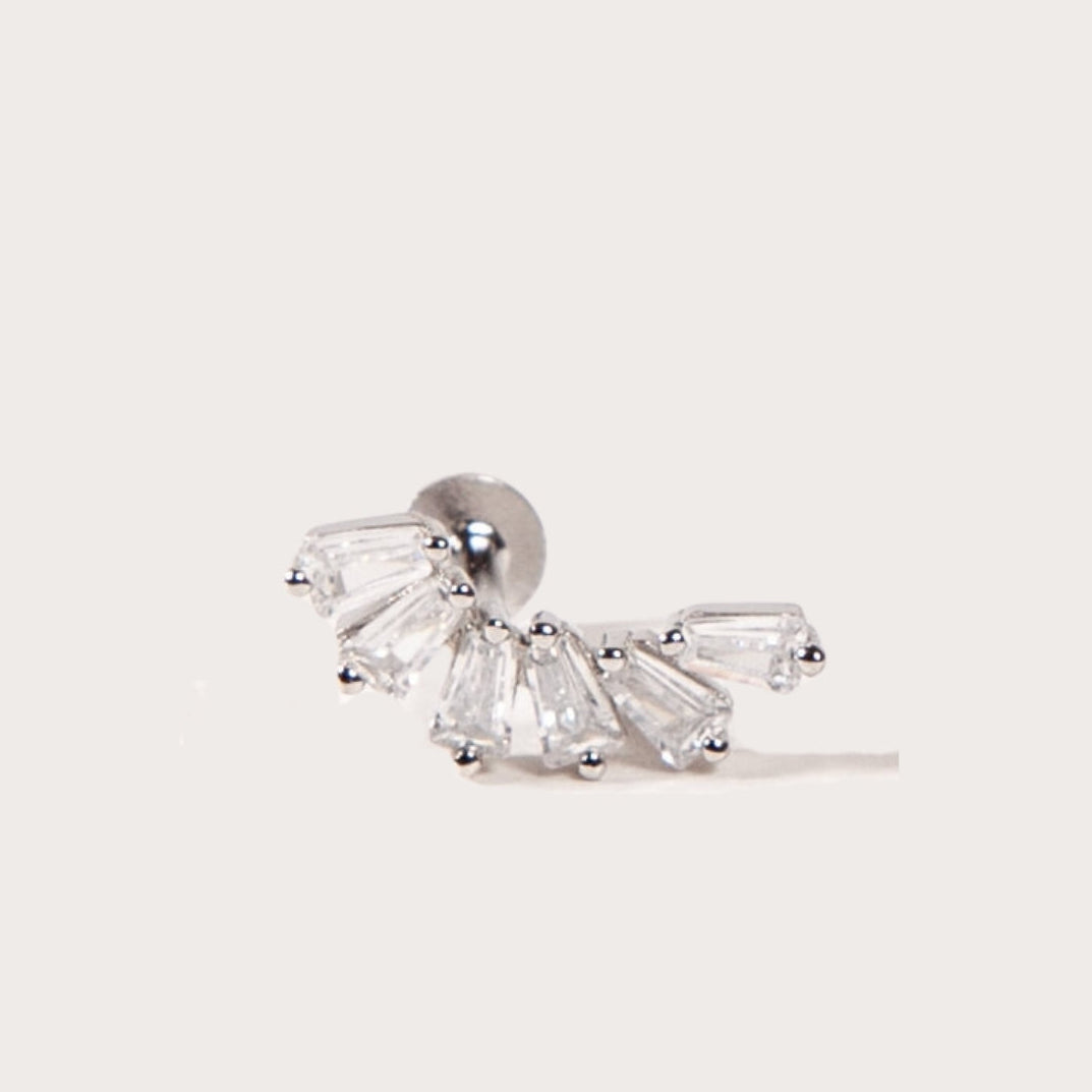 A silver crown-like shape with baguette-cut stones stud earring on a light beige background
