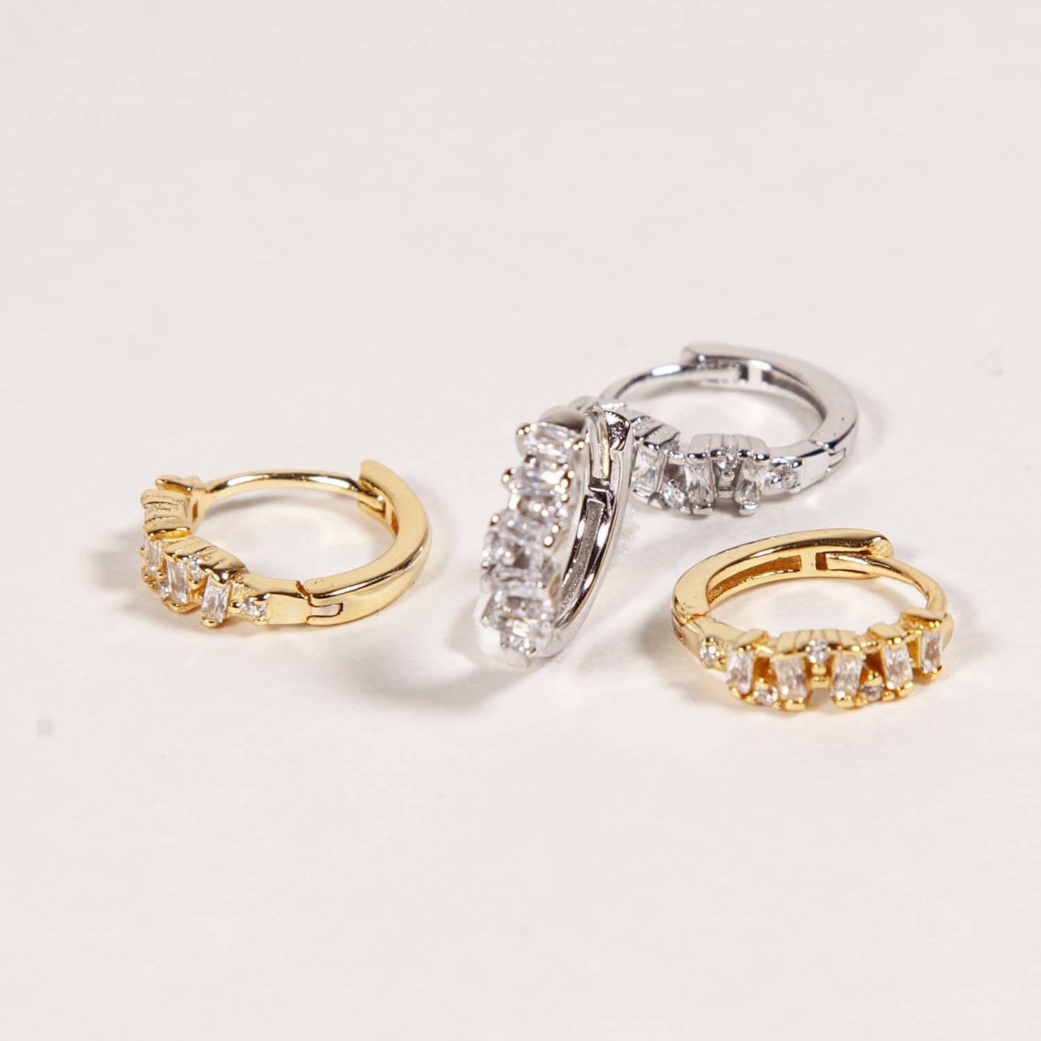 Gold and silver huggies with baguette CZ stones on a white background